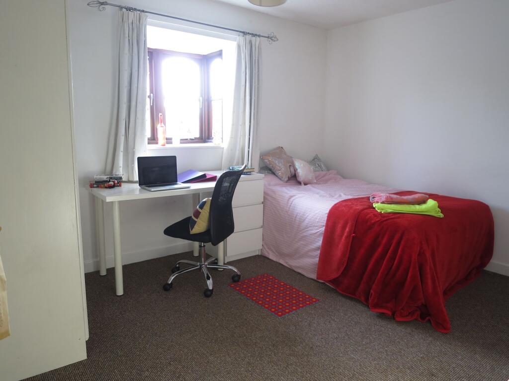 A cozy single bedroom featuring a bed with pink...