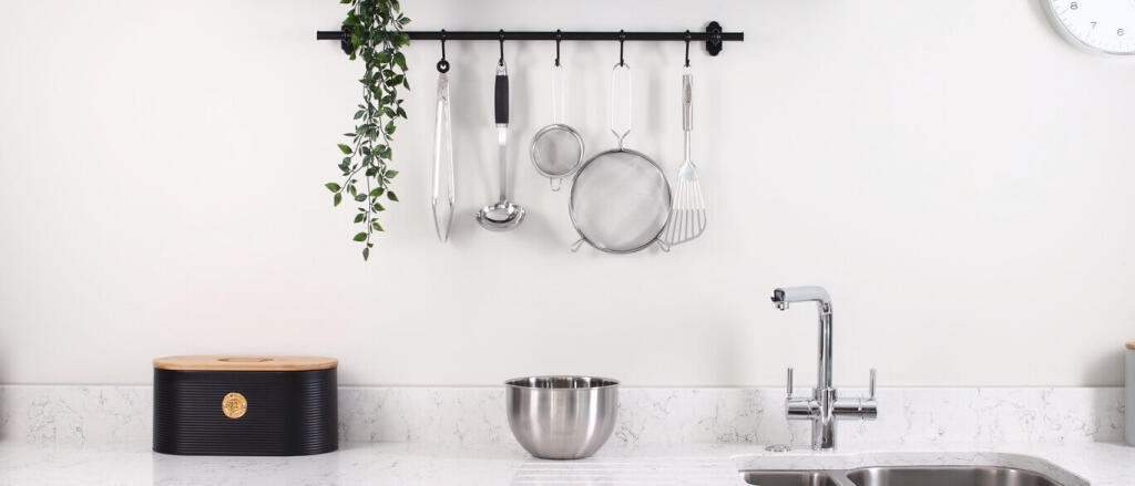 Modern kitchen with white marble countertop, stainless steel bowl, hanging utensils, and a small pla