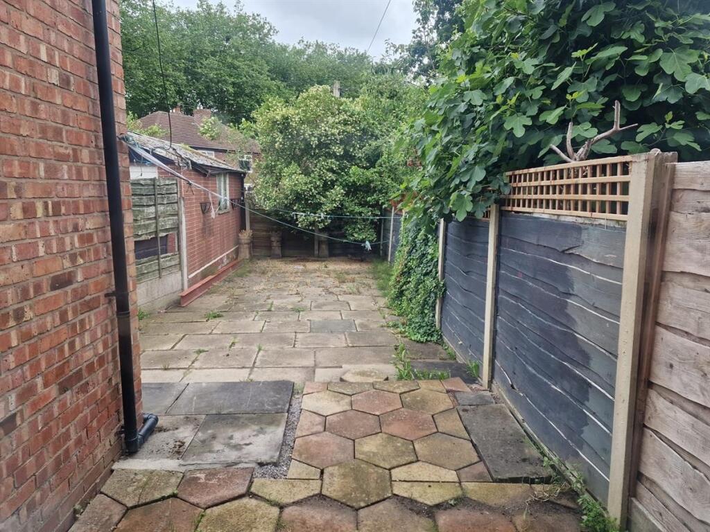 Paved rear garden with mature greenery and fenc...