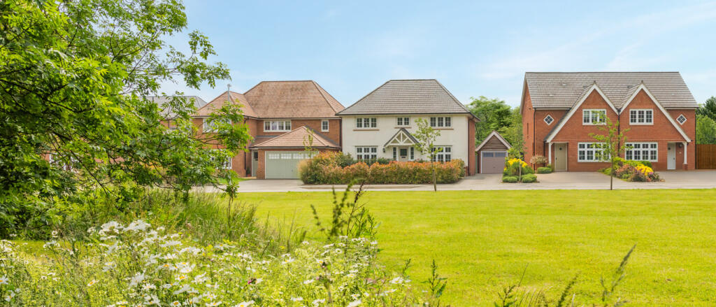 Three modern detached houses with well-maintained lawns and trees in a suburban neighbourhood under