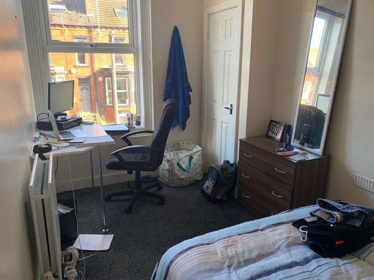 A well-lit bedroom featuring a bed, a desk with...