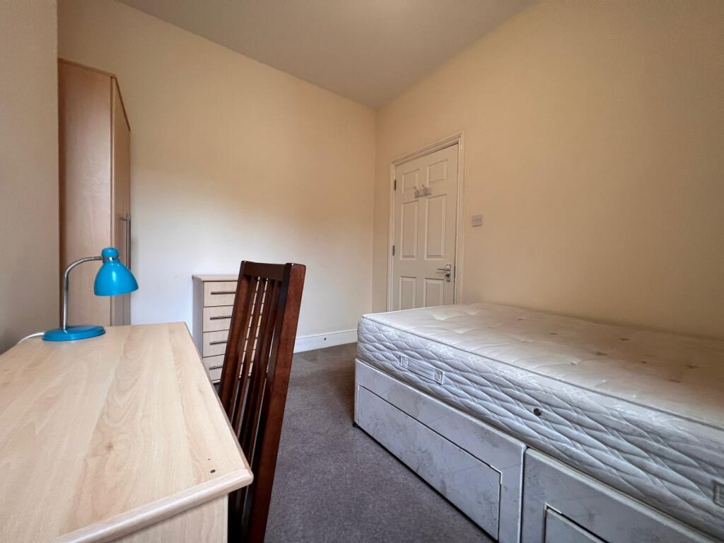 A cozy single bedroom featuring a wooden desk w...