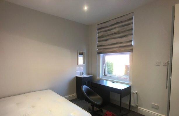 A well-lit, tidy bedroom featuring a comfortabl...