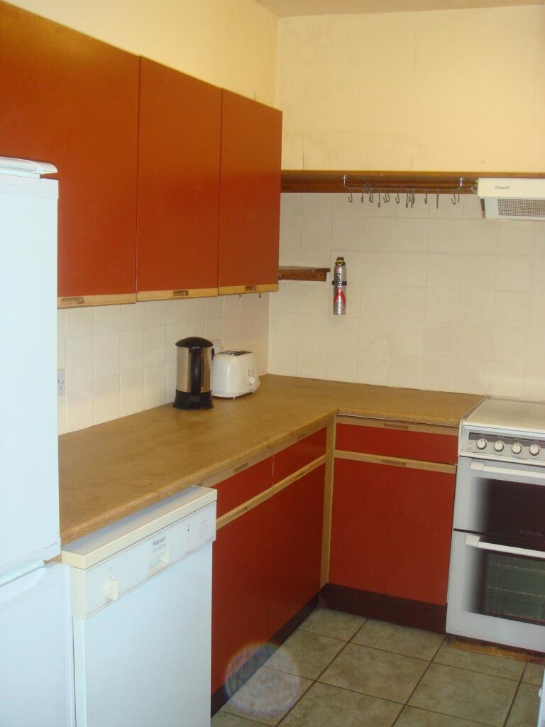 A compact, functional kitchen with warm red cab...