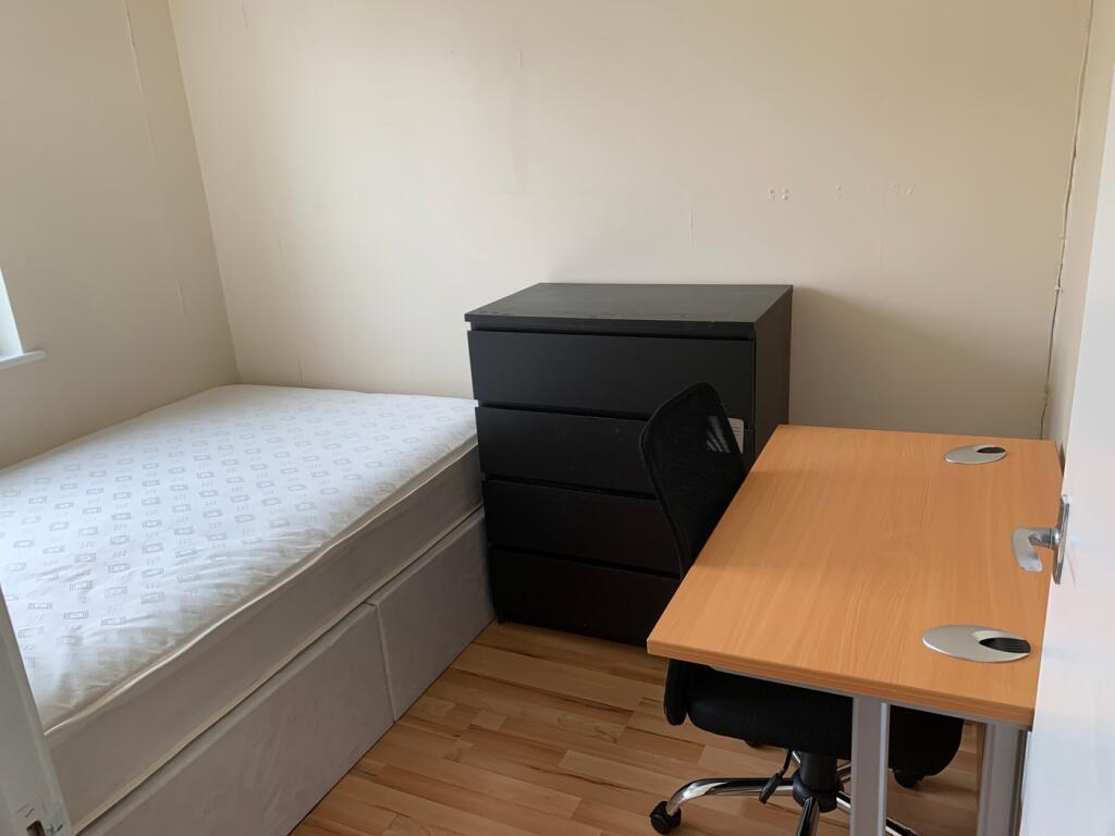 A tidy single bedroom with a comfortable desk a...