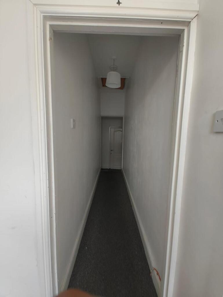 A narrow hallway with white walls and dark floo...