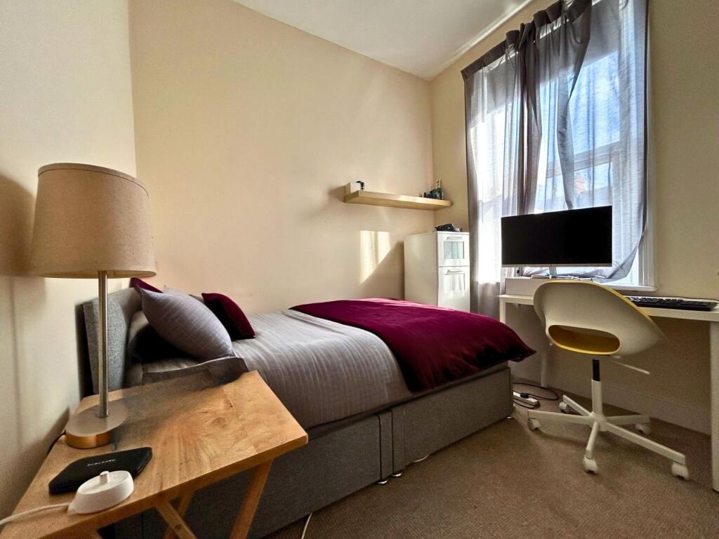 A cozy, well-lit single bedroom featuring a com...