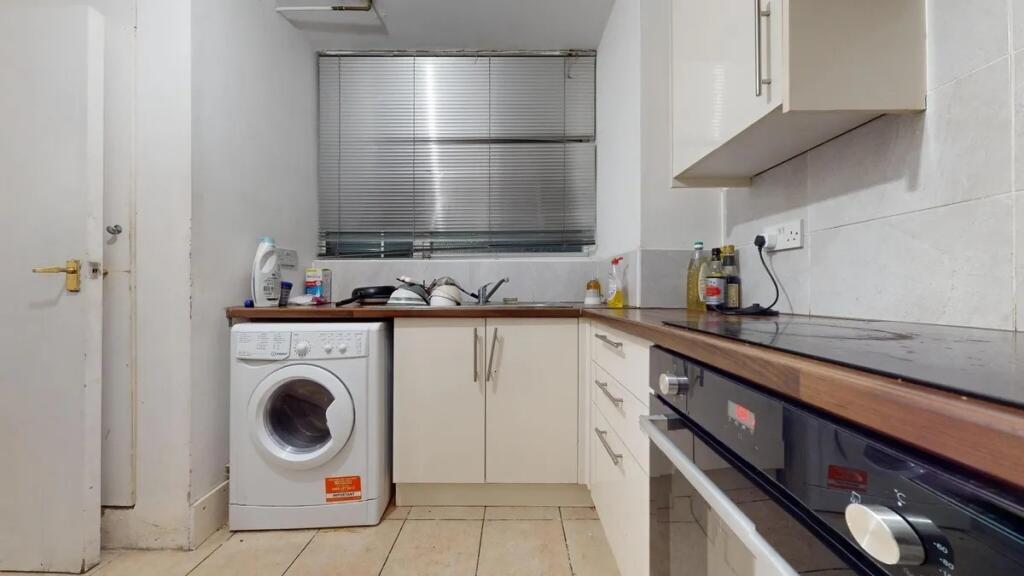 A compact kitchen featuring modern white cabine...