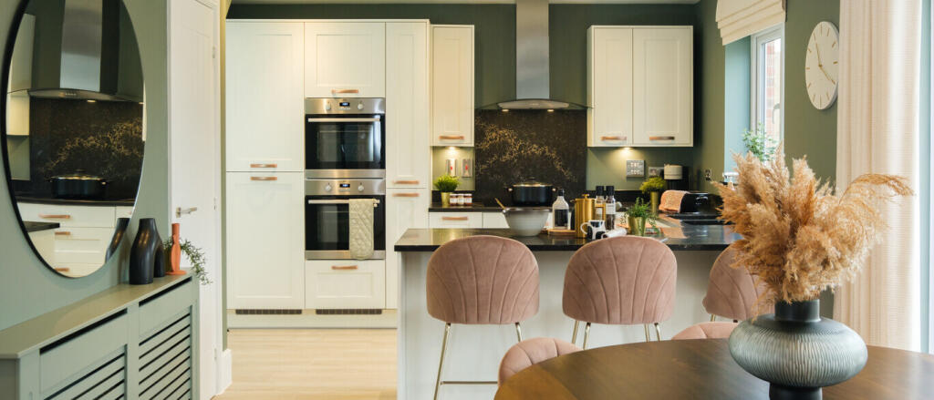 Modern kitchen and dining area with cream cabinets, pink chairs, and a vase with dried flowers on a