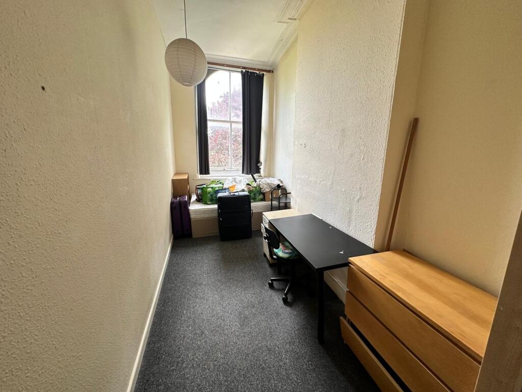 A cozy single bedroom with a desk and storage, ...