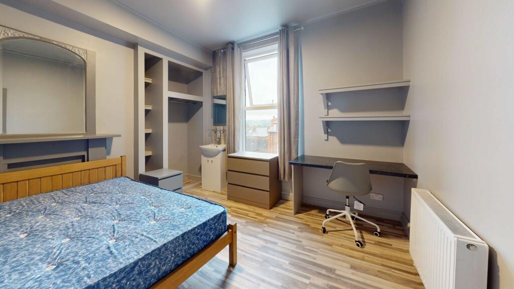 A well-lit single bedroom featuring a wooden be...