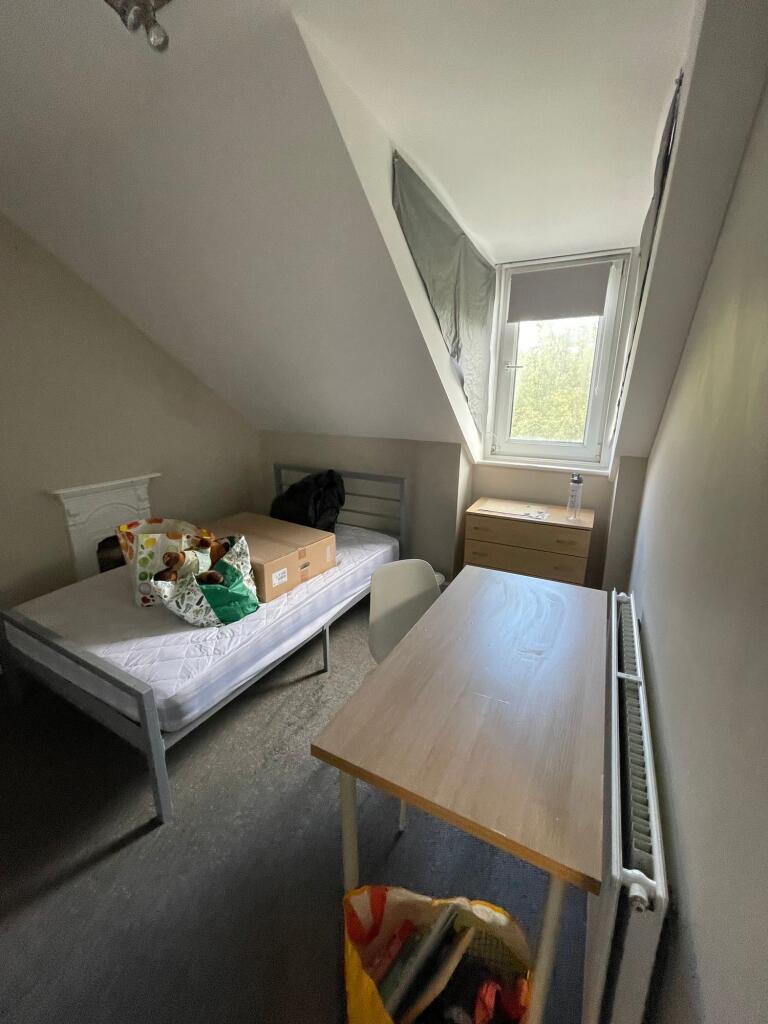 A compact room featuring a simple bed with a sm...
