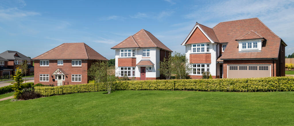 Two modern detached houses with white and brick facades, surrounded by a green lawn and hedge, under