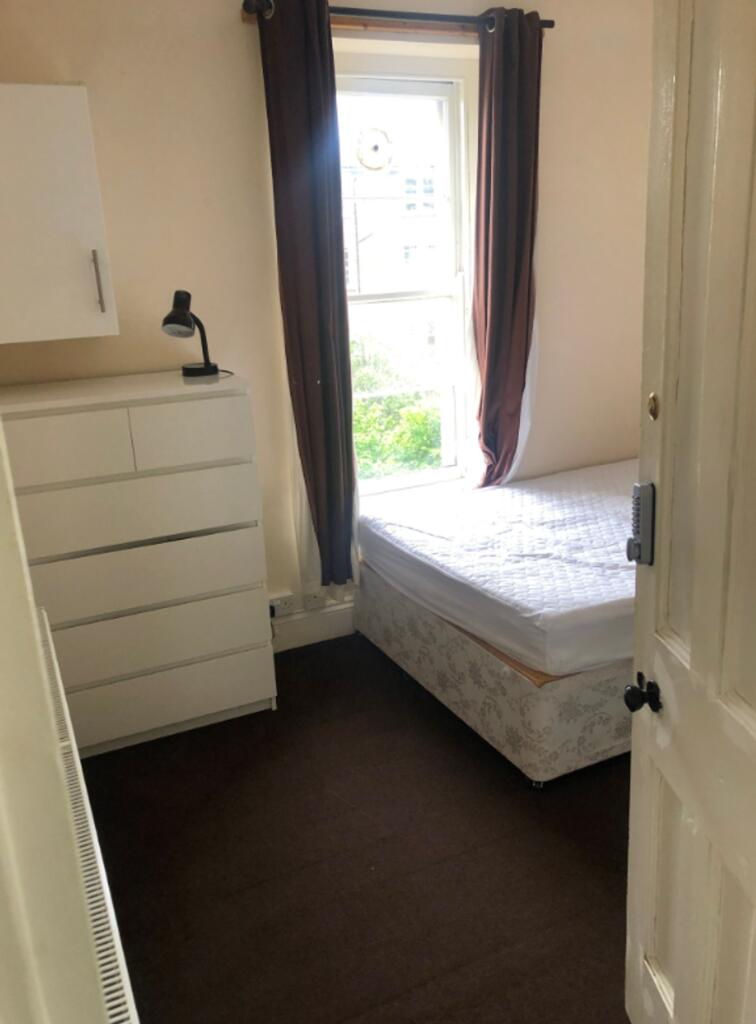 A tidy single bedroom with a bed and a dresser,...