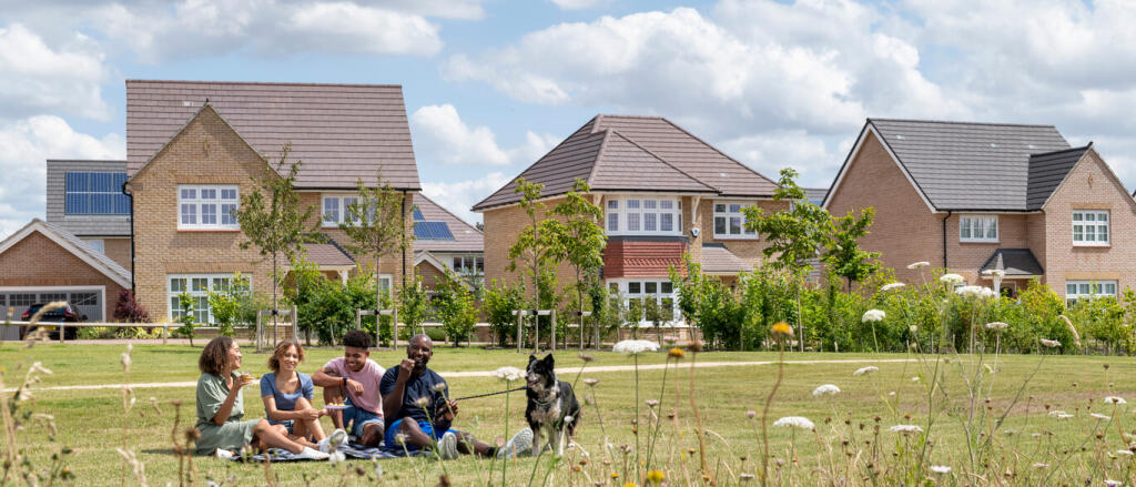 Group of children and a dog enjoying a picnic on a grassy field in front of modern suburban houses u