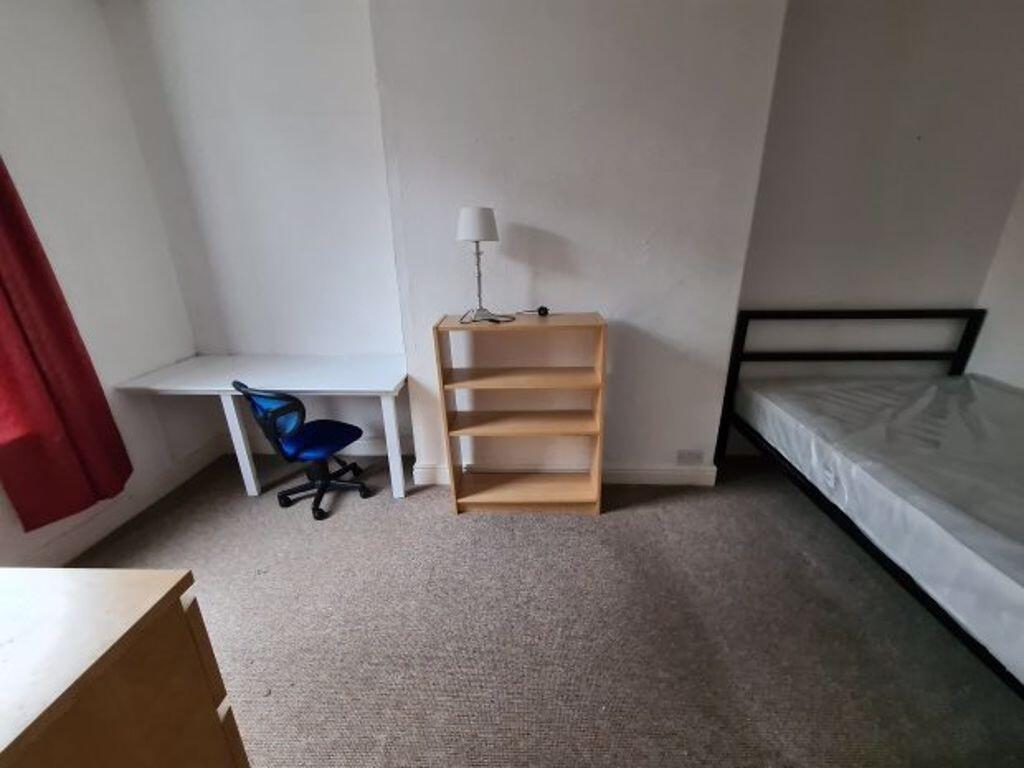 A tidy single bedroom featuring a bed, a desk w...