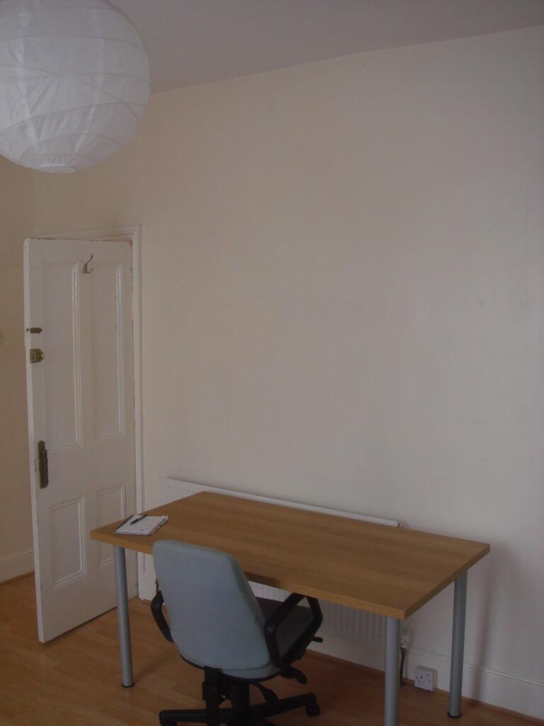 A simple, tidy bedroom with a wooden desk and a...