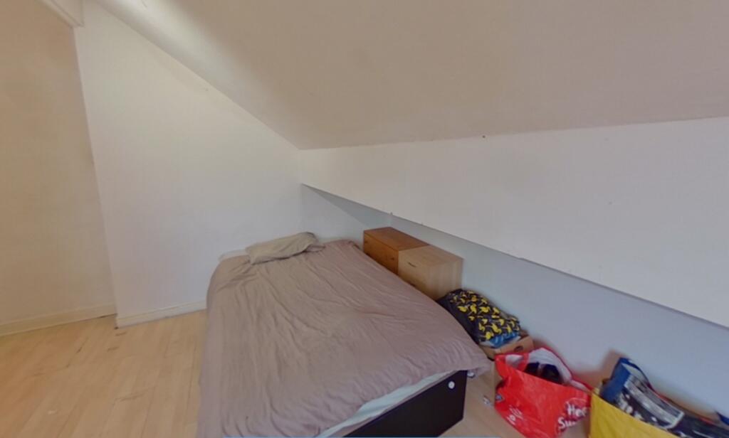 A modest single bedroom featuring a slanted cei...