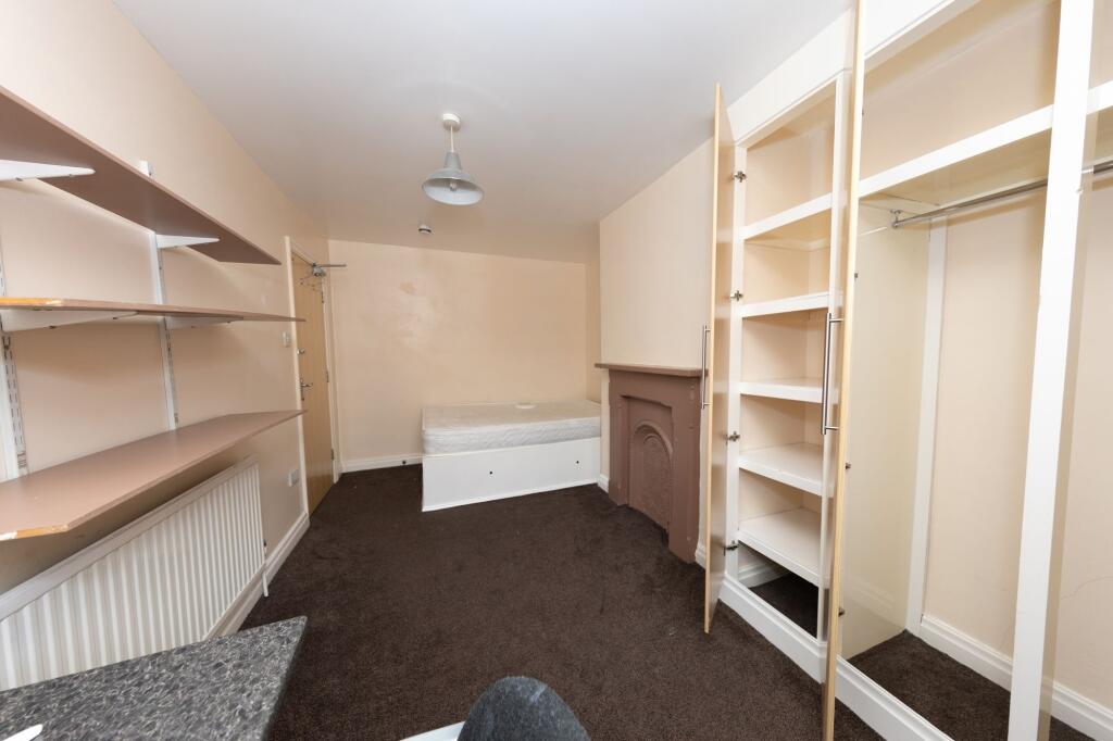 A modest bedroom featuring shelves, a radiator,...