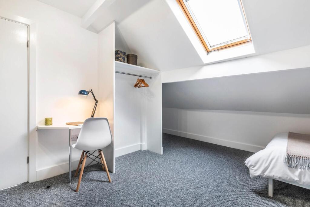 A well-lit, tidy single bedroom featuring a des...