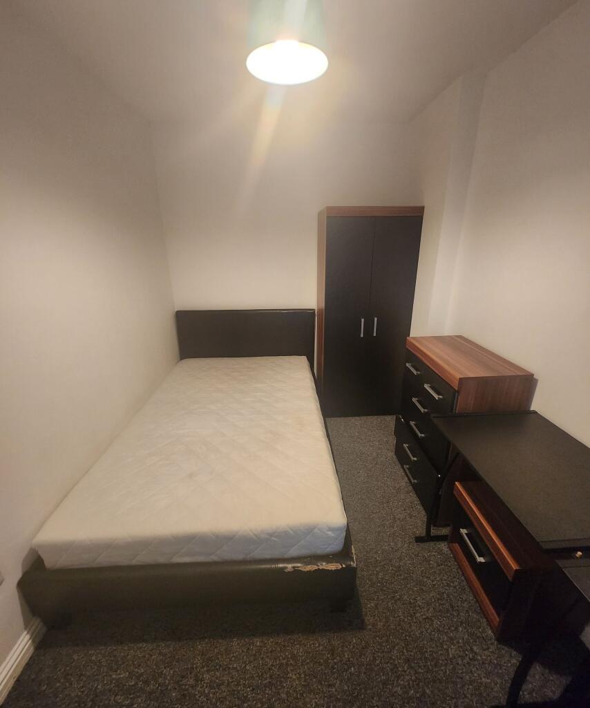 A compact single bedroom featuring a bed with a...