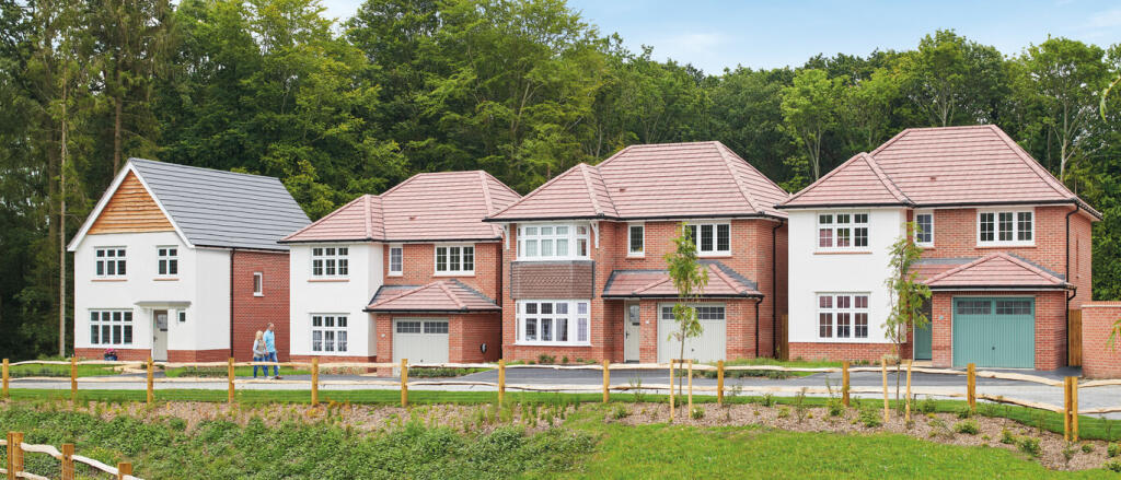 Newly built houses with red brick and white exteriors, some with bay windows, set against a green wo