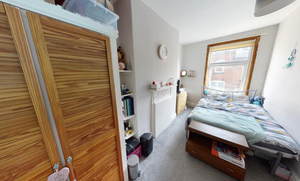 A cozy single bedroom featuring a bed, a window...