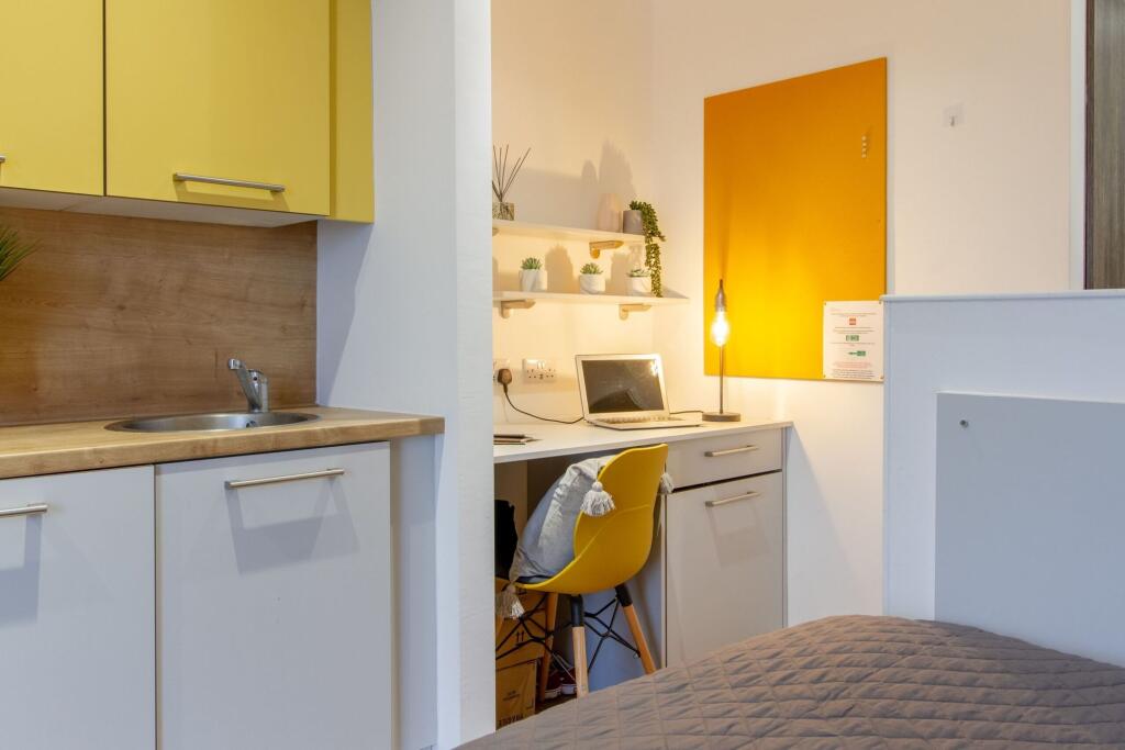 A cozy single bedroom featuring a compact kitch...