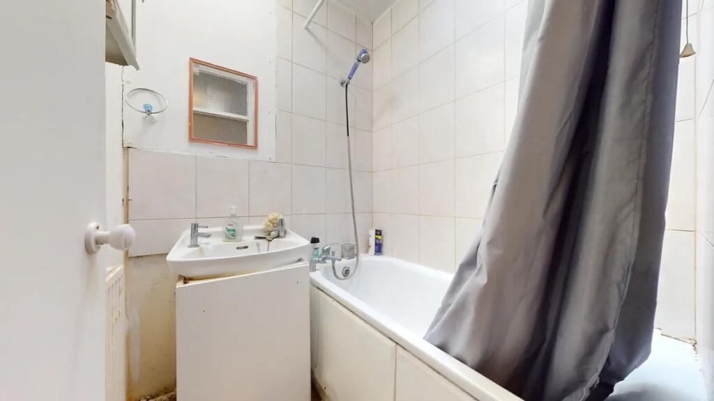 Compact bathroom featuring a bathtub with showe...