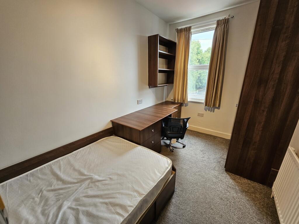 A cozy single bedroom featuring a bed, a wooden...