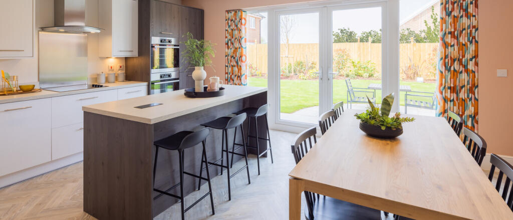 Modern kitchen and dining area with large glass doors opening to a garden, featuring white cabinetry