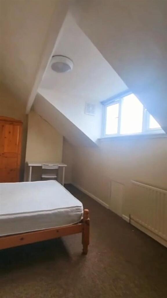 A cozy single bedroom featuring a slanted ceili...