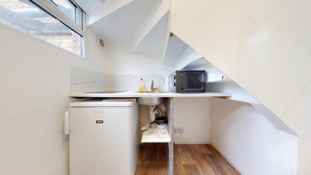 Compact kitchen space featuring a small fridge,...