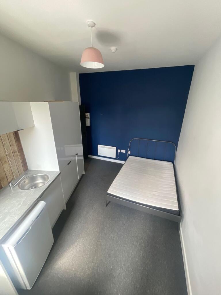 A tidy single bedroom featuring a compact kitch...