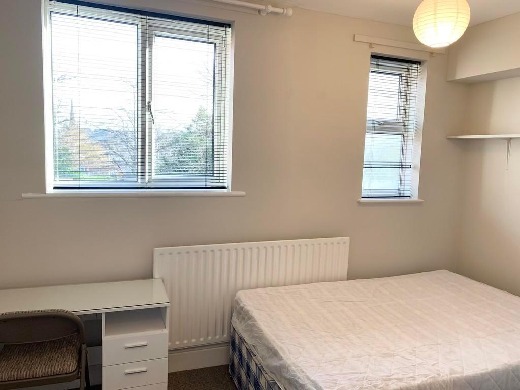 A bright double bedroom featuring two large win...
