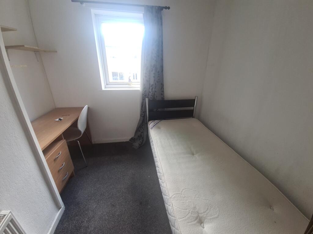 A compact bedroom featuring a single bed with a...