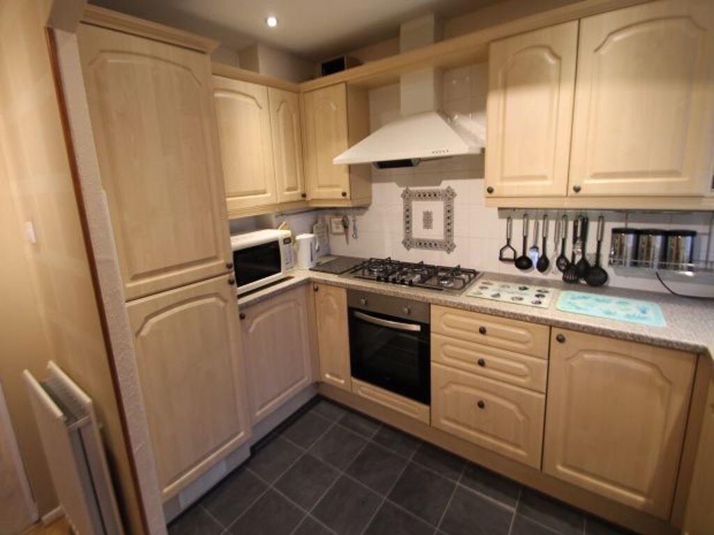 Warm, well-equipped kitchen with light wood cab...