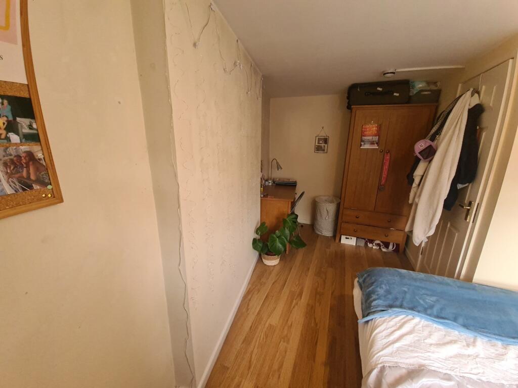 A cozy single bedroom featuring a wooden floor,...