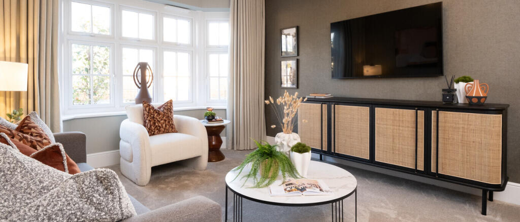 Spacious living room with a large bay window, beige and grey furniture, a flat-screen TV, and decora