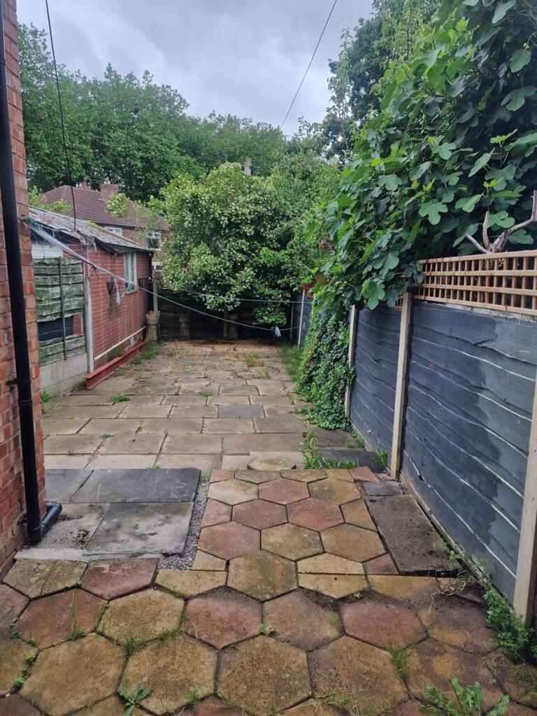 Private paved rear garden with mature trees and...