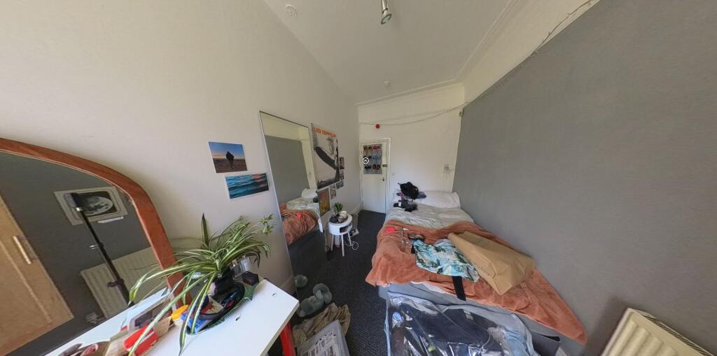 A cozy single bedroom featuring a bright worksp...