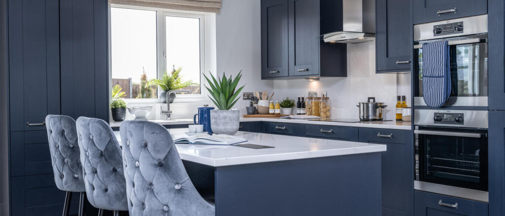 Modern kitchen with navy blue cabinets, white island and grey upholstered chairs under a window with