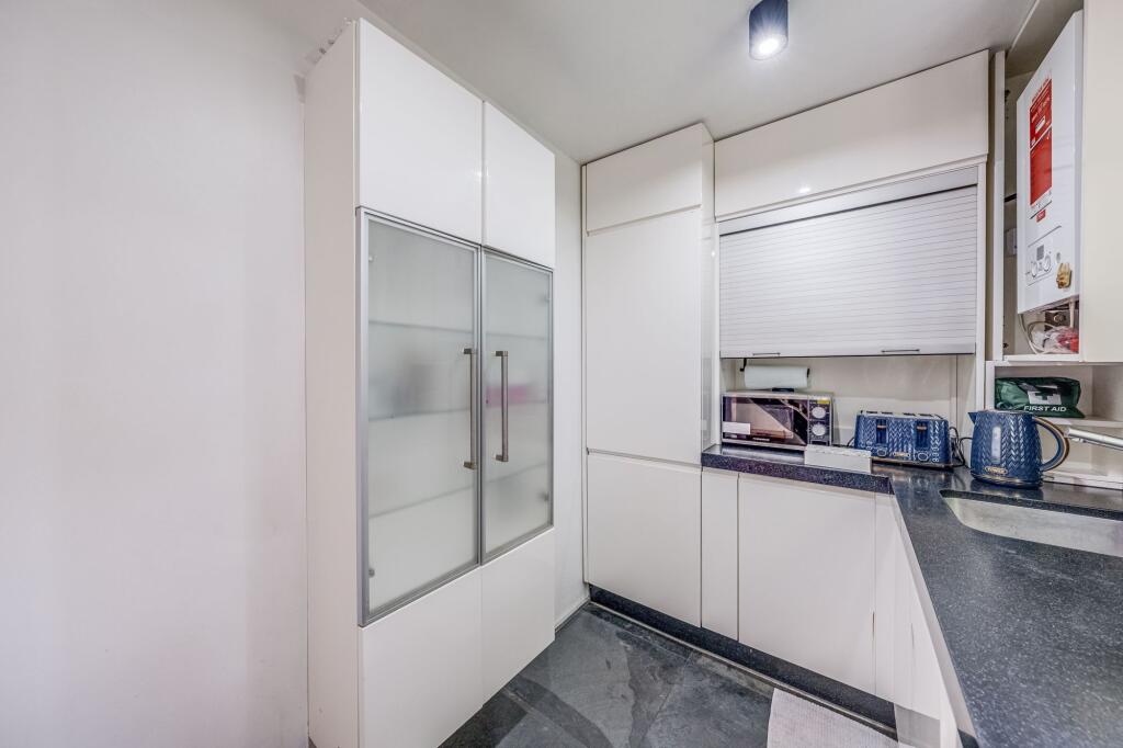 A modern, compact kitchen featuring sleek white...