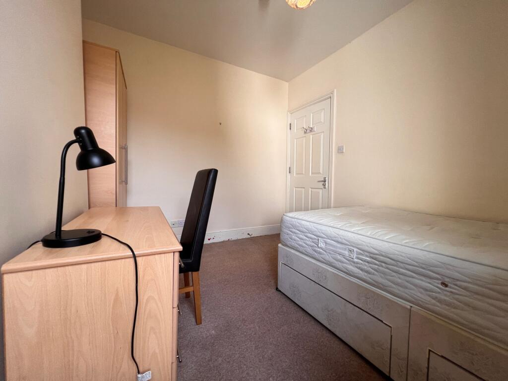 A tidy single bedroom featuring a wooden desk w...