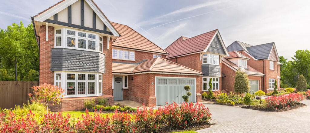 Modern semi-detached houses with red brick and grey tiled roofs, surrounded by colourful gardens and
