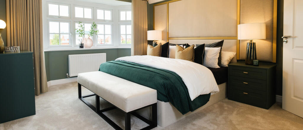 Elegant bedroom with large bay window, beige and dark green decor, and a neatly made bed with multip