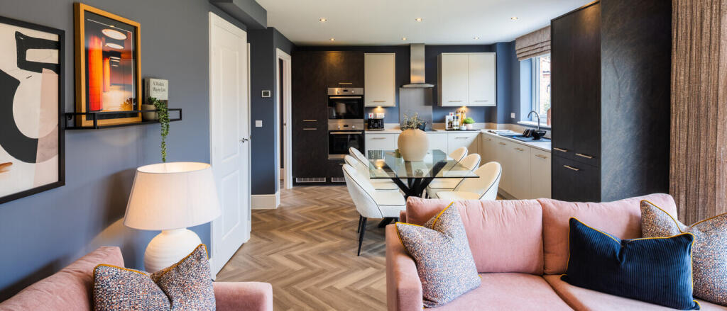 Modern open-plan living room and kitchen with grey walls, white cabinets,, pink sofa, and wooden flo
