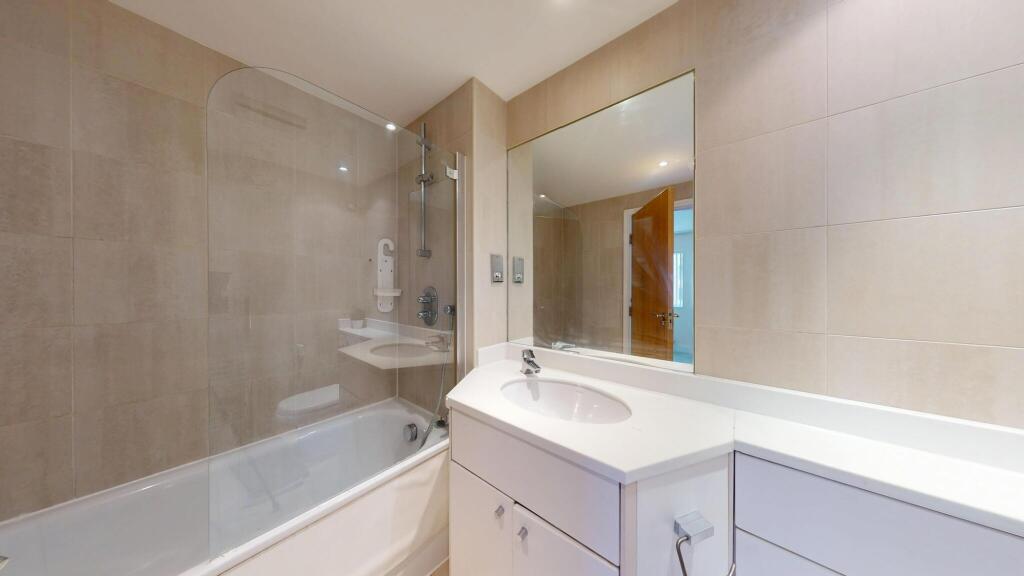 A modern bathroom featuring a bathtub with a gl...