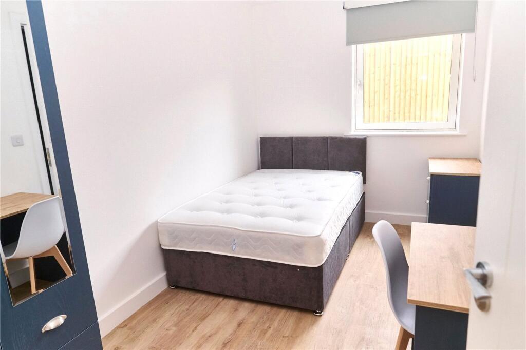 A neat and well-lit small bedroom with a comfor...
