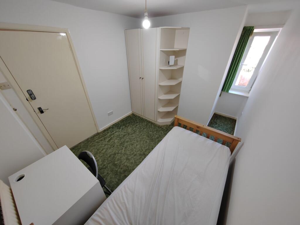 A cozy single bedroom with a simple bed frame, ...